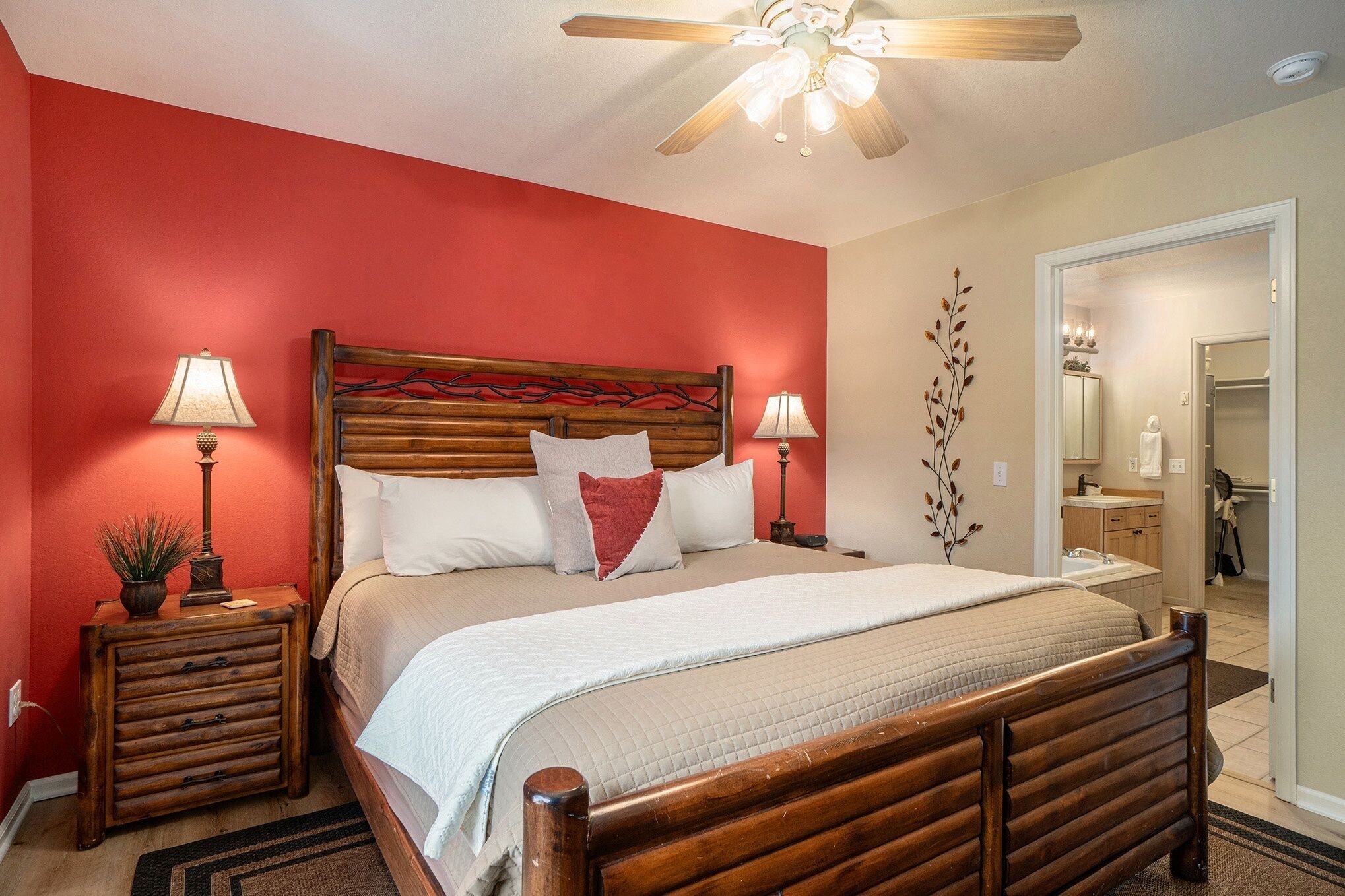 A bedroom with a wooden bed, red walls, two bedside tables with lamps, and a ceiling fan.