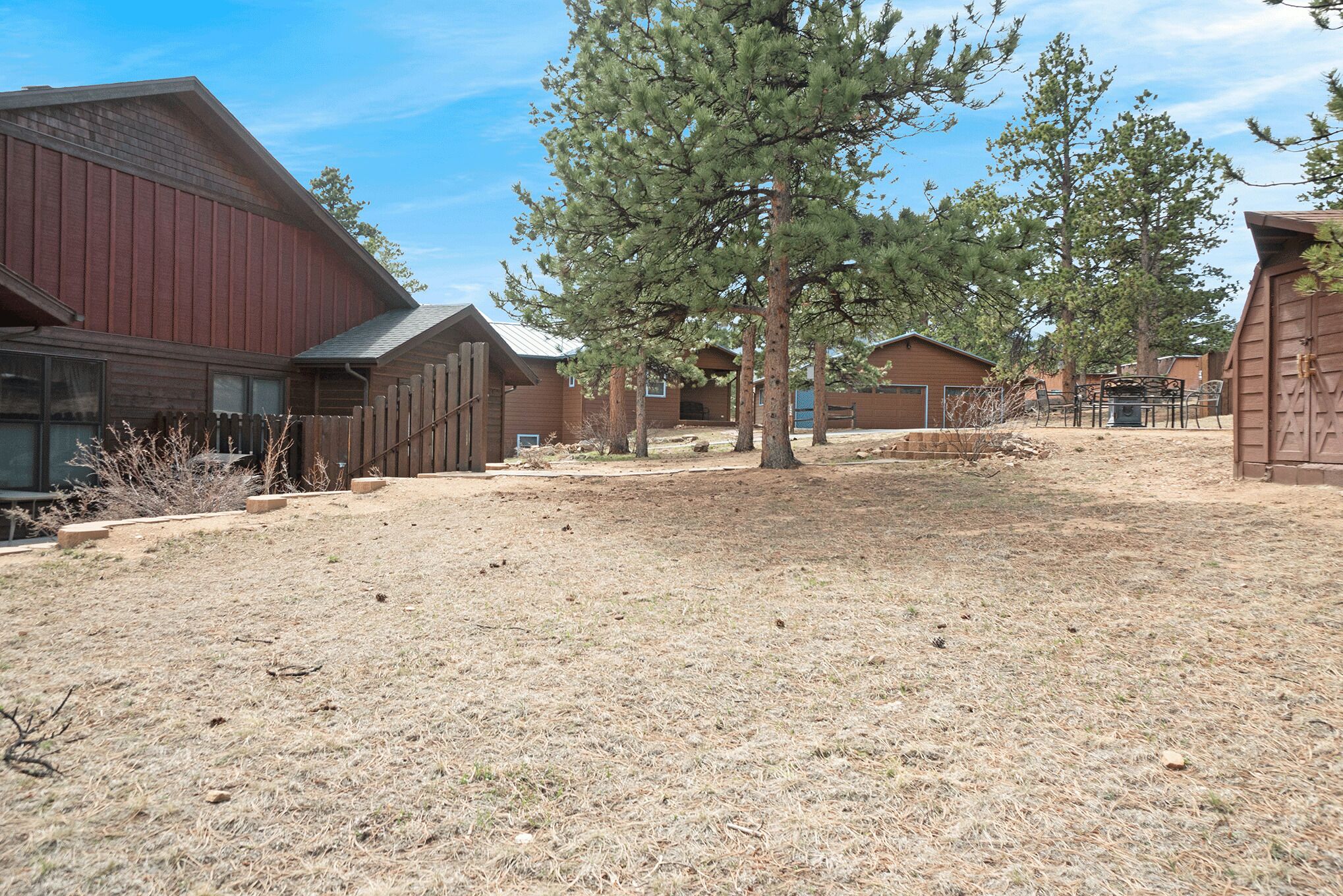 A dry, grassy area with wooden buildings and a large pine tree.