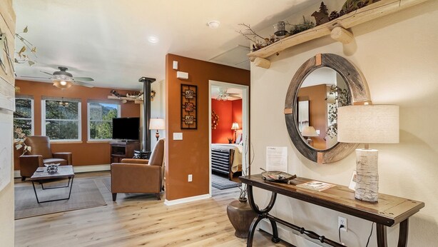 A spacious living room with hardwood flooring, a ceiling fan, a large mirror, and a television.