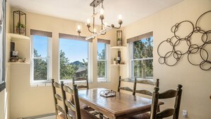 A dining room with a wooden table and chairs, a chandelier, and large windows with views of trees and hills.