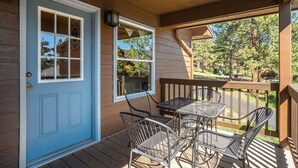 A wooden deck with a blue door, a table with chairs, and a view of the surrounding trees.