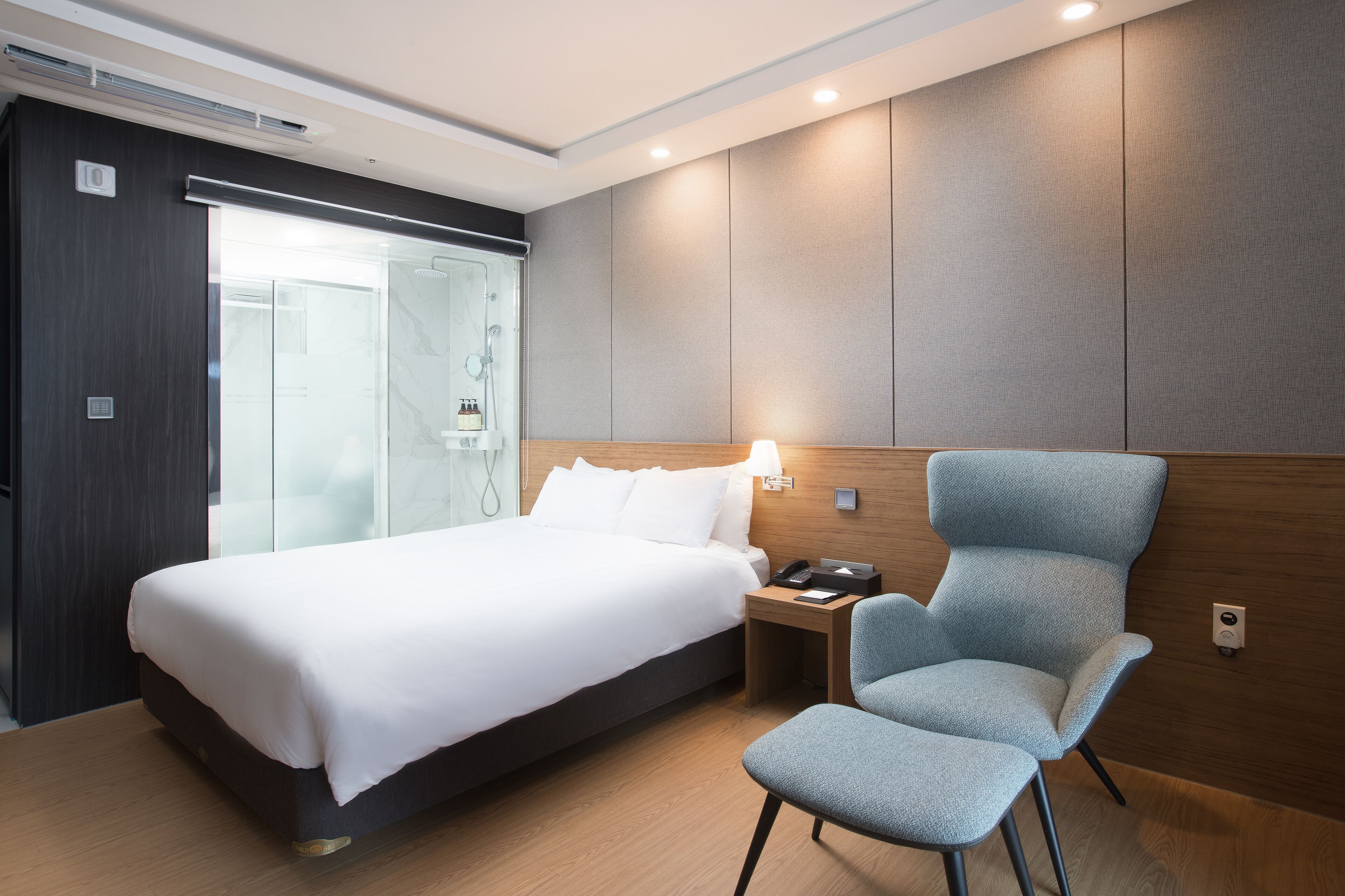 A modern hotel room with a large bed, a seating area, and a glass shower enclosure.