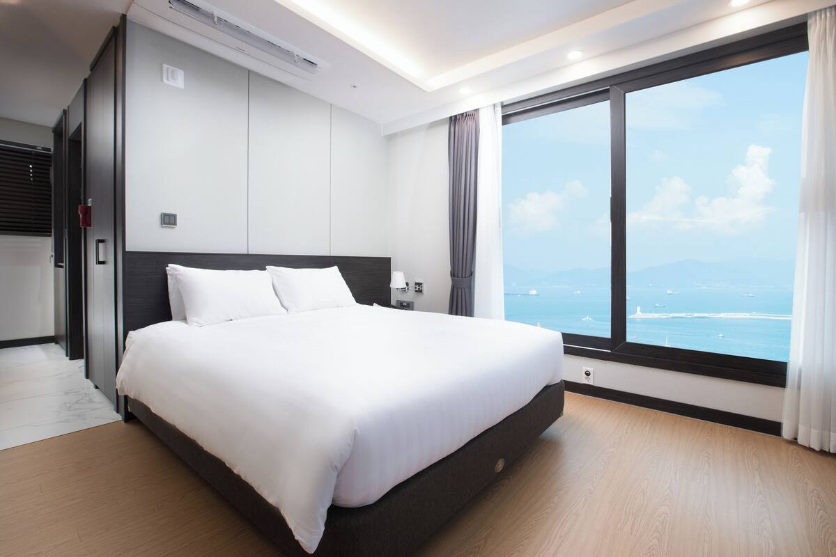 Een moderne hotelkamer met een groot bed, een nachtkastje, een raam met uitzicht op zee en een grote spiegel.
