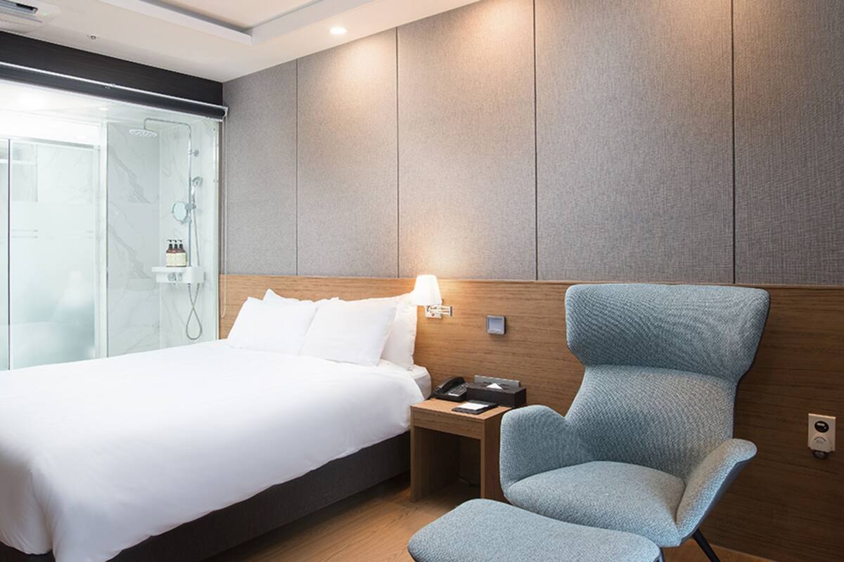 Een hotelkamer met een bed, een stoel, een nachtkastje en een douchecabine van glas.