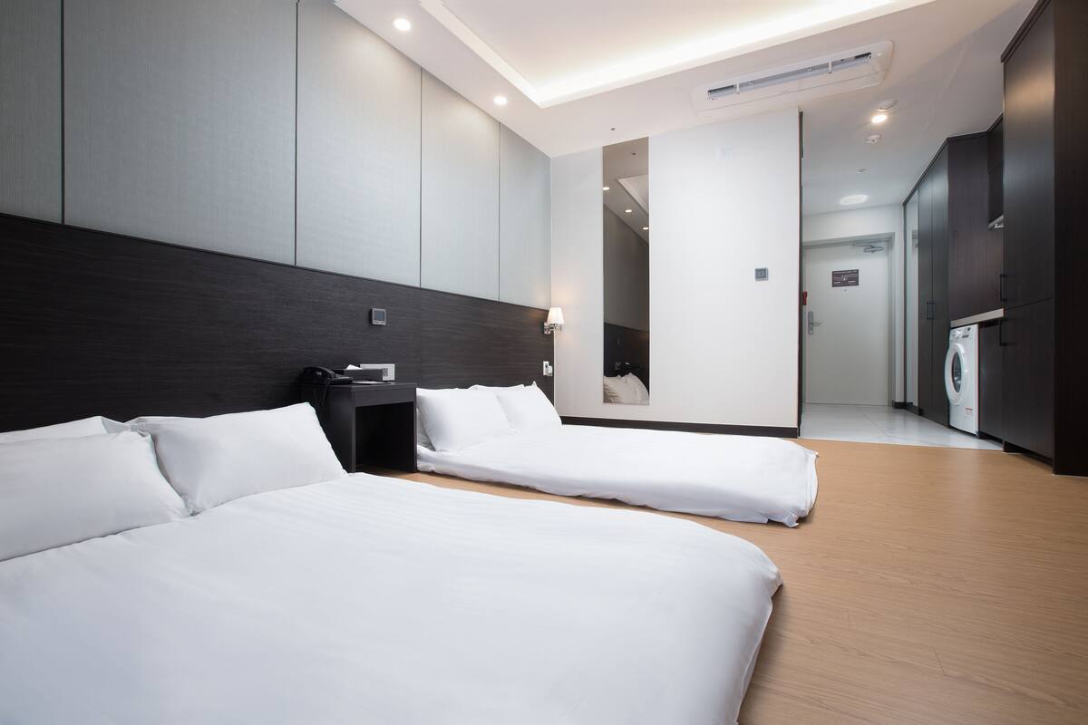 Een moderne hotelkamer met twee eenpersoonsbedden, een nachtkastje, een lamp en uitzicht op de hal.
