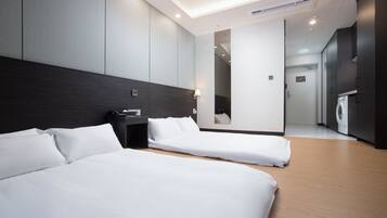 Habitación de hotel moderna con dos camas individuales, una mesita de noche, una lámpara y vistas al pasillo.