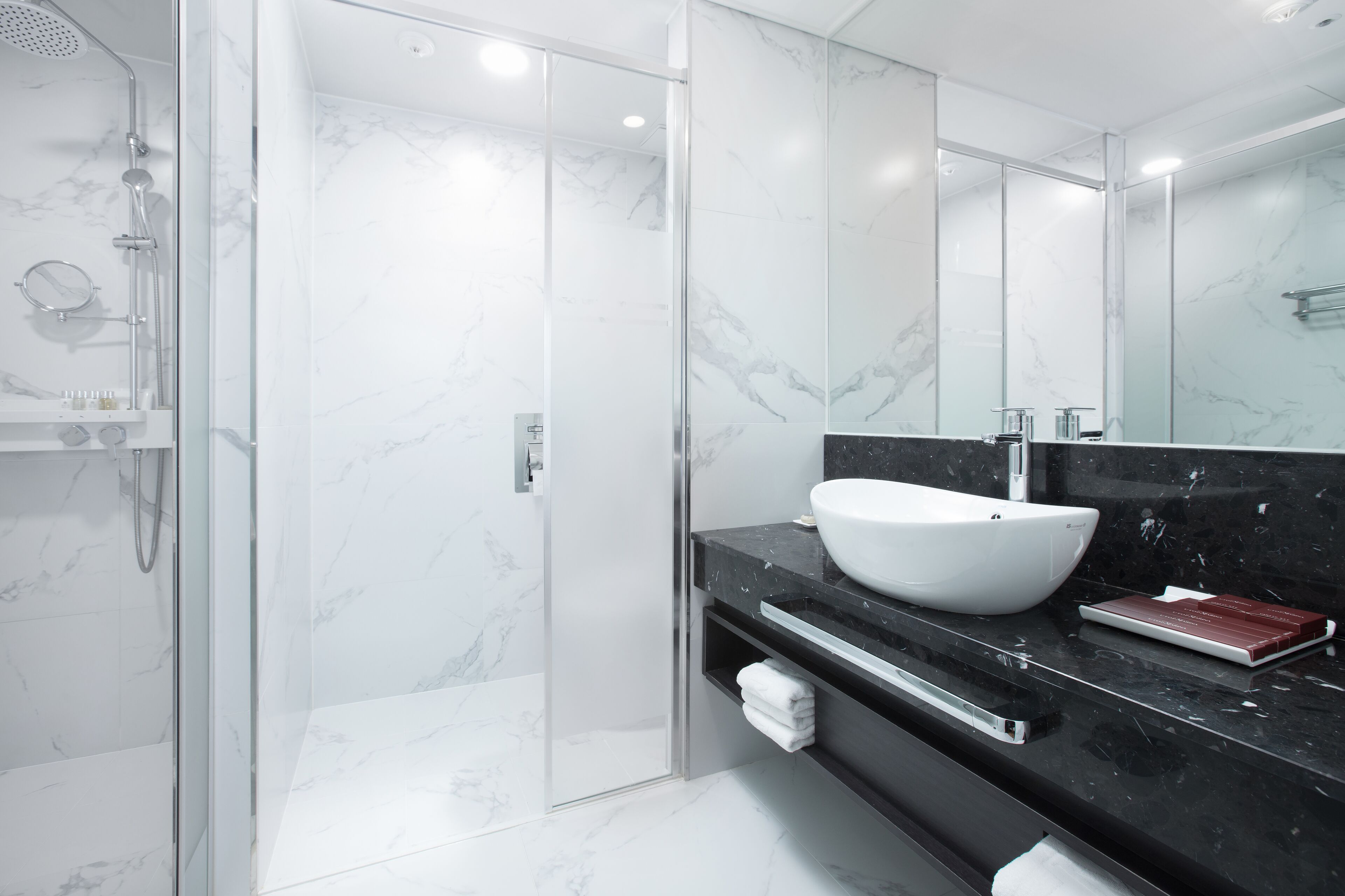 A modern bathroom with a glass-enclosed shower, a white marble sink, and a large mirror.