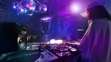 A DJ booth with a Pioneer DJ controller, a Pioneer DJ speaker, and a disco ball in a dimly lit room with purple lighting.