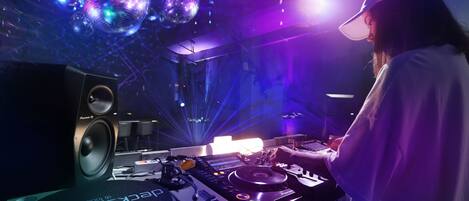 A DJ booth with a Pioneer DJ controller, a Pioneer DJ speaker, and a disco ball in a dimly lit room with purple lighting.