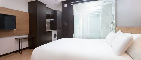 Una habitación de hotel moderna con una cama grande, un televisor de pantalla plana en la pared, lavadora integrada y cabina de ducha de vidrio.
