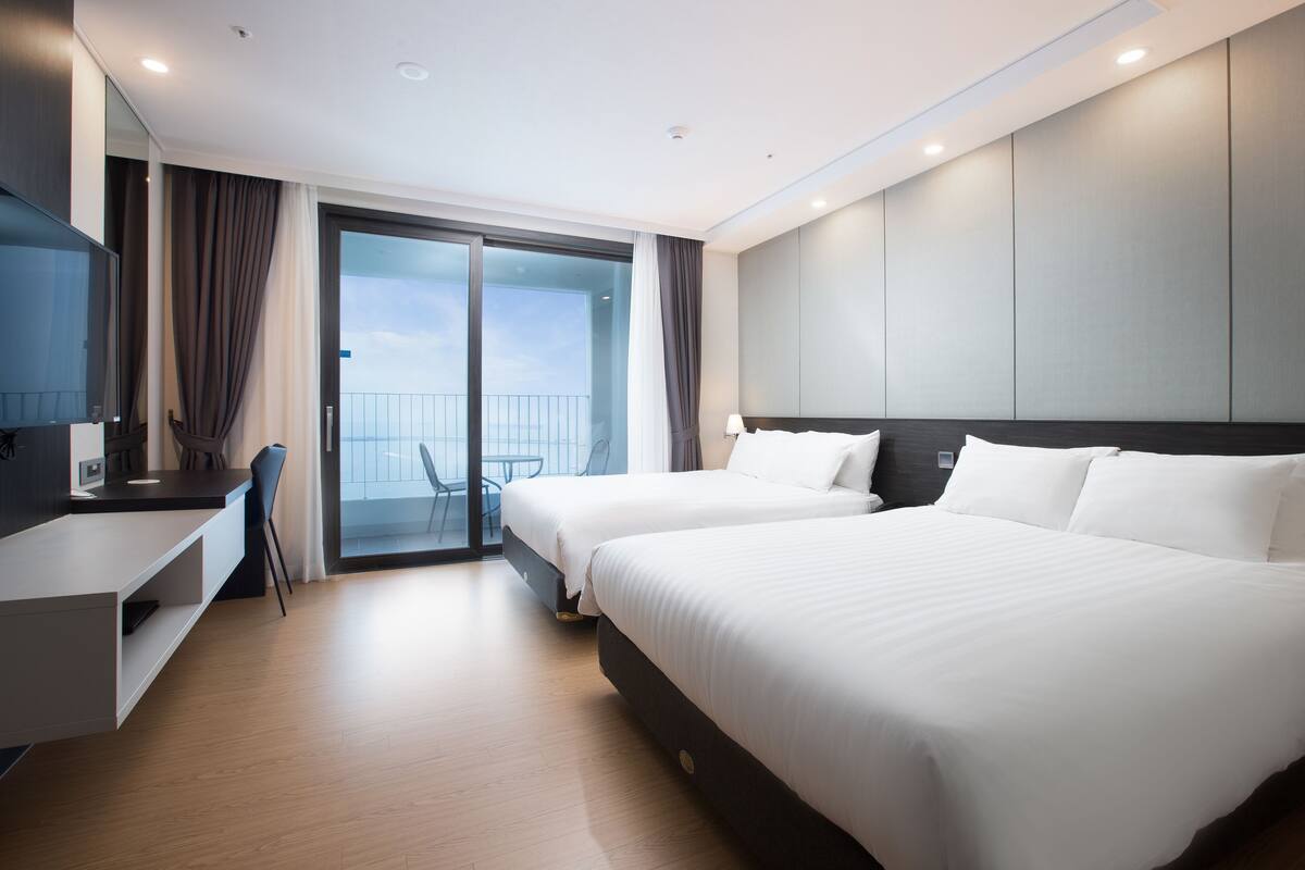 Een moderne hotelkamer met twee bedden, een bureau en een balkon met uitzicht.