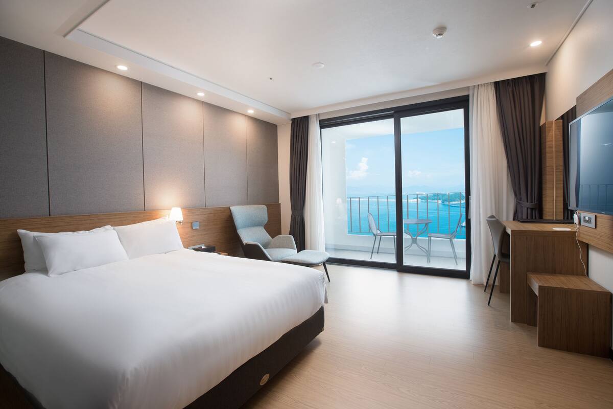 Een moderne hotelkamer met een groot bed, een bureau en een balkon met uitzicht op zee.