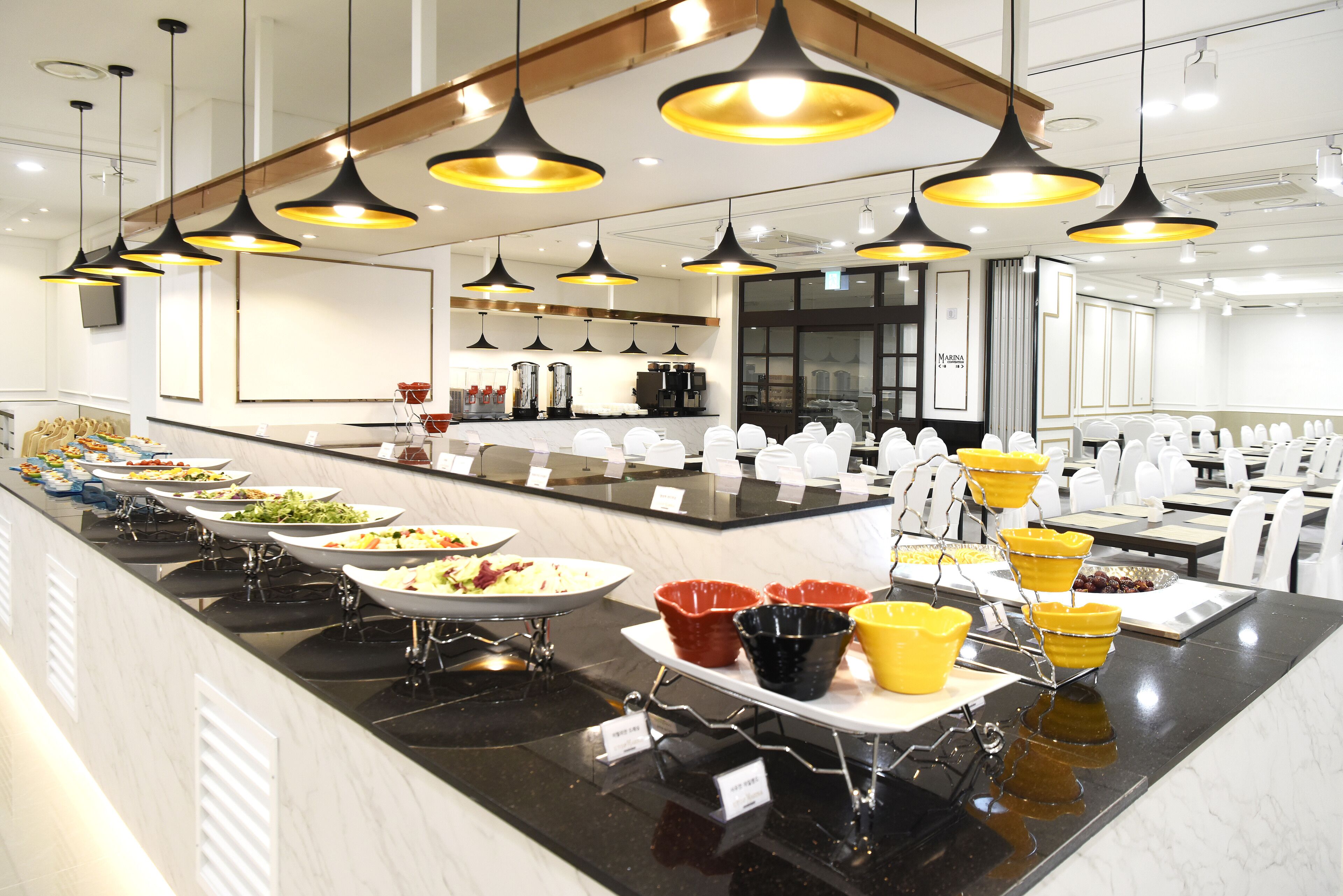 A buffet setup with multiple serving stations, a coffee machine, and a seating area with chairs.