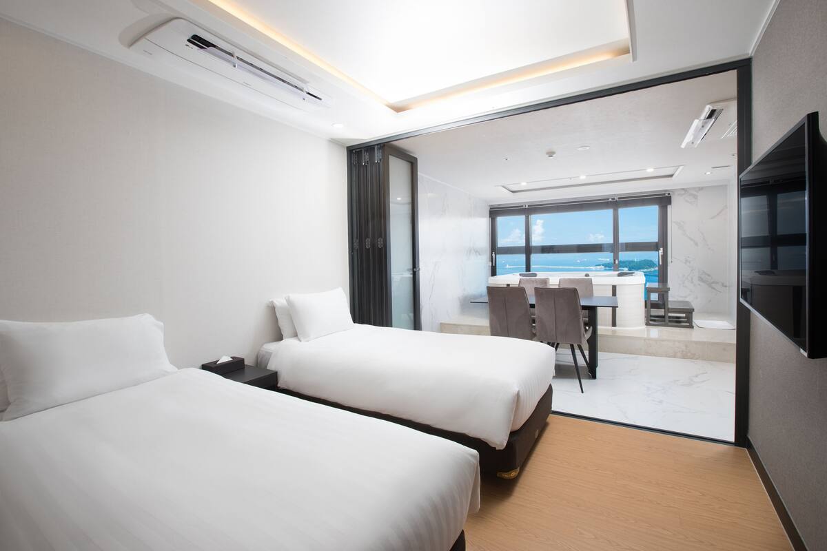 Een moderne hotelkamer met twee bedden, een bureau en uitzicht op zee.