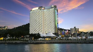 A high-rise hotel with multiple floors, a waterfront view, and a prominent building in the background. - Utop Marina Hotel & Resort (Yeosu)