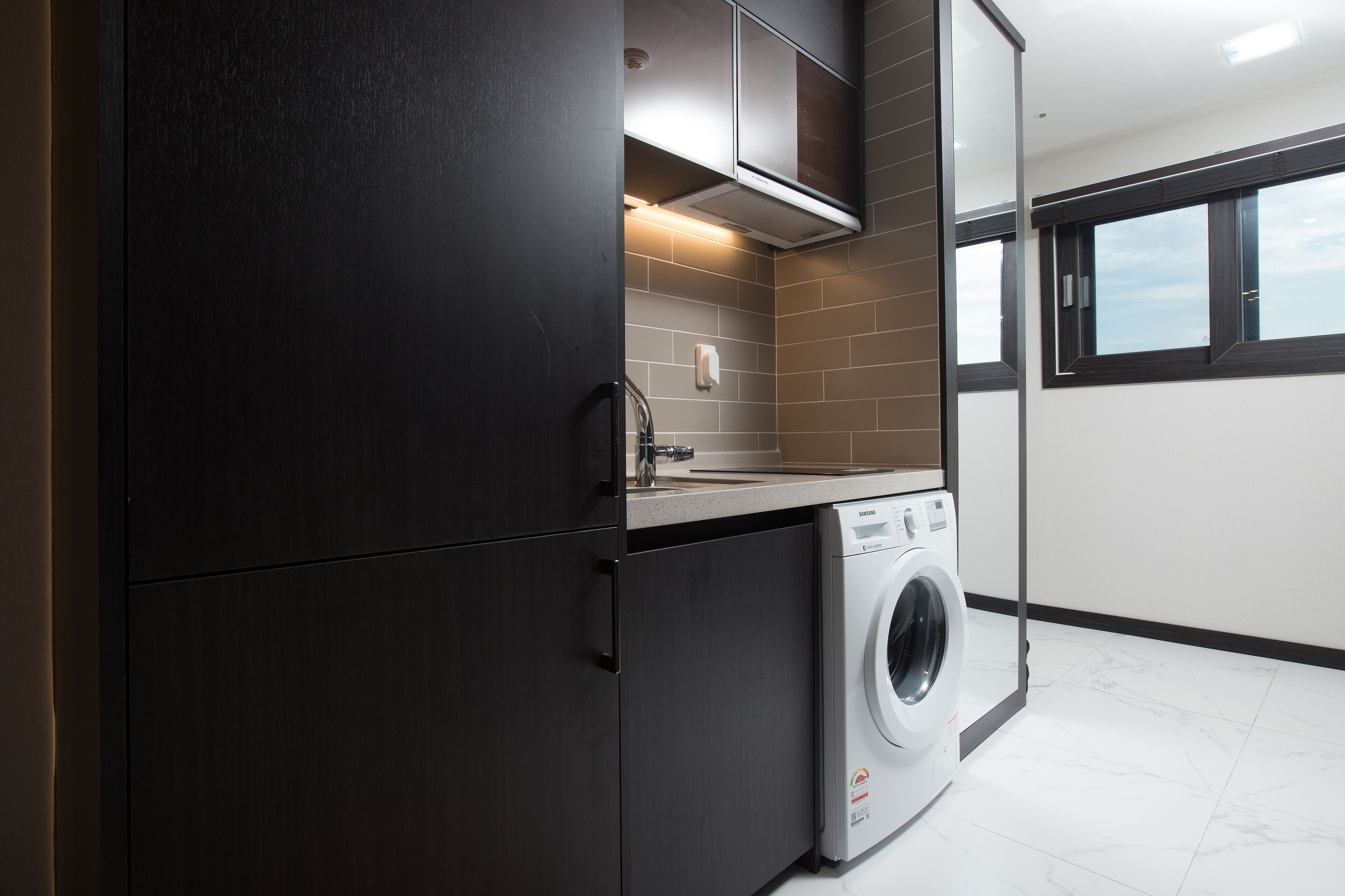 A modern laundry room with a washing machine, dark cabinets, and a window.