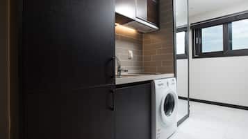 A modern laundry room with a washing machine, dark cabinets, and a window.