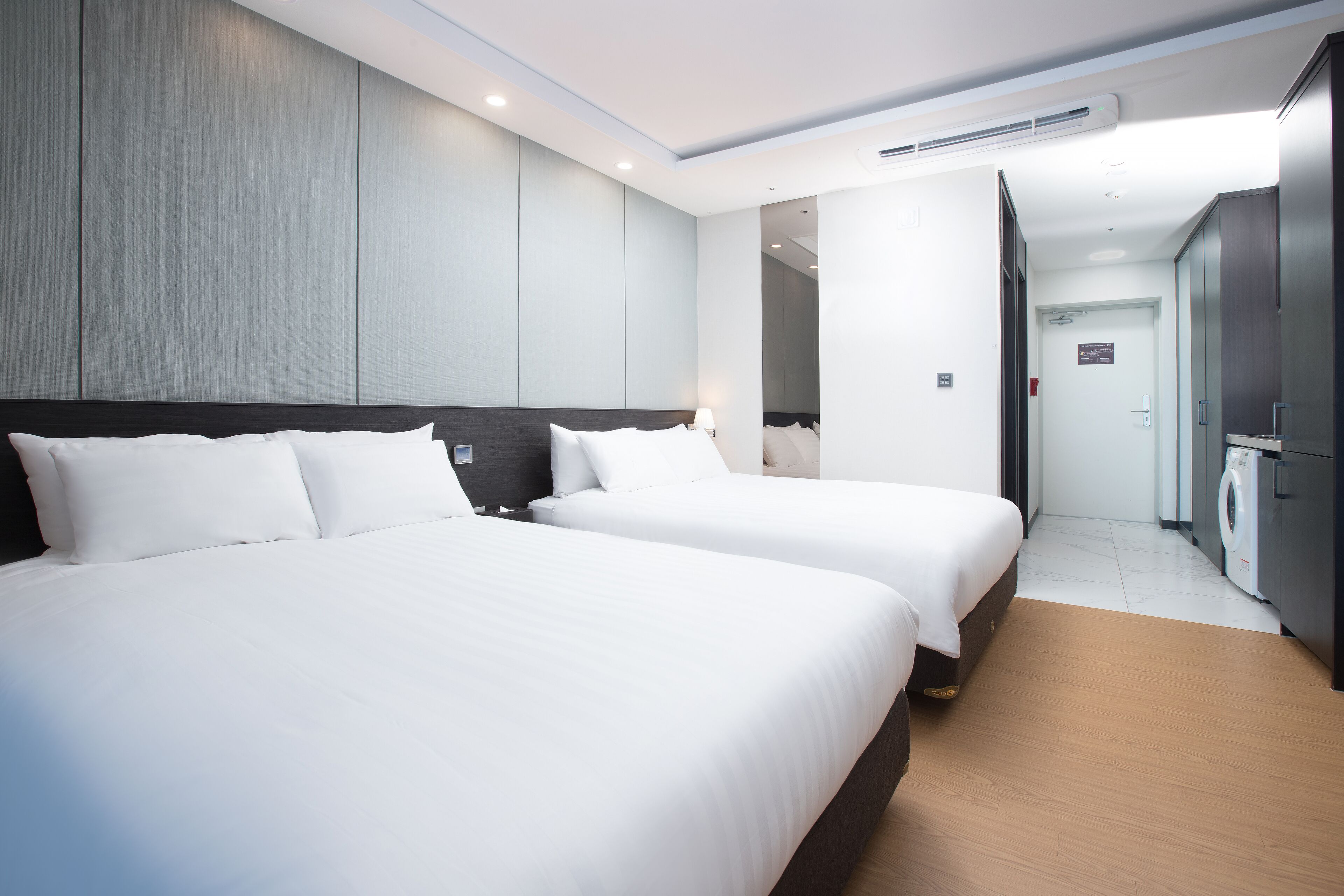 A hotel room with two beds, a wardrobe, and a washing machine.