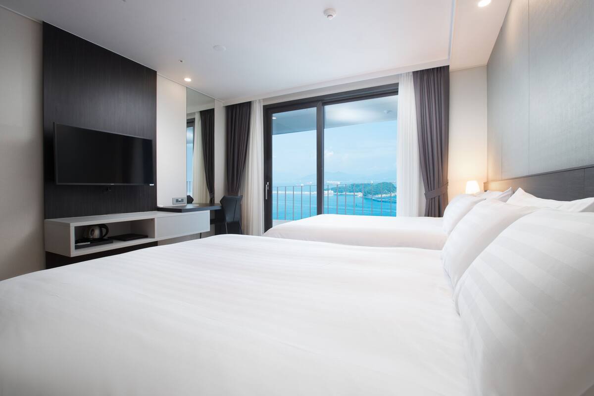 Een moderne hotelkamer met een groot bed, een flatscreen-tv aan de muur en een balkon met uitzicht op zee.