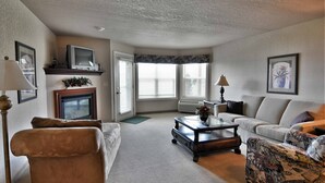 A living room with a fireplace, a sofa, a patterned armchair, and a television on a stand. - Unit 312 1 Bd/ 1 Ba Condo 1 Bedroom Condo by RedAwning (Birchwood)