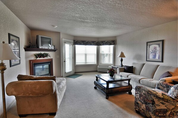 A living room with a fireplace, a sofa, a patterned armchair, and a television on a stand. - Unit 312 1 Bd/ 1 Ba Condo 1 Bedroom Condo by RedAwning (Birchwood)
