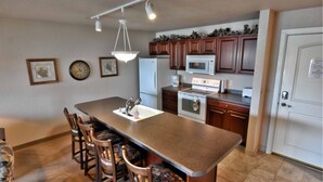 A kitchen with a central island, wooden cabinets, a refrigerator, microwave, and a stove. - Unit 312 1 Bd/ 1 Ba Condo 1 Bedroom Condo by RedAwning (Birchwood)