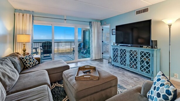 A living room with a large TV, comfortable seating, and a view to the outside. - Amelia by the Sea Oceanfront Condo with Access to Private Fishing Pier by RedAwning (Fernandina Beach)