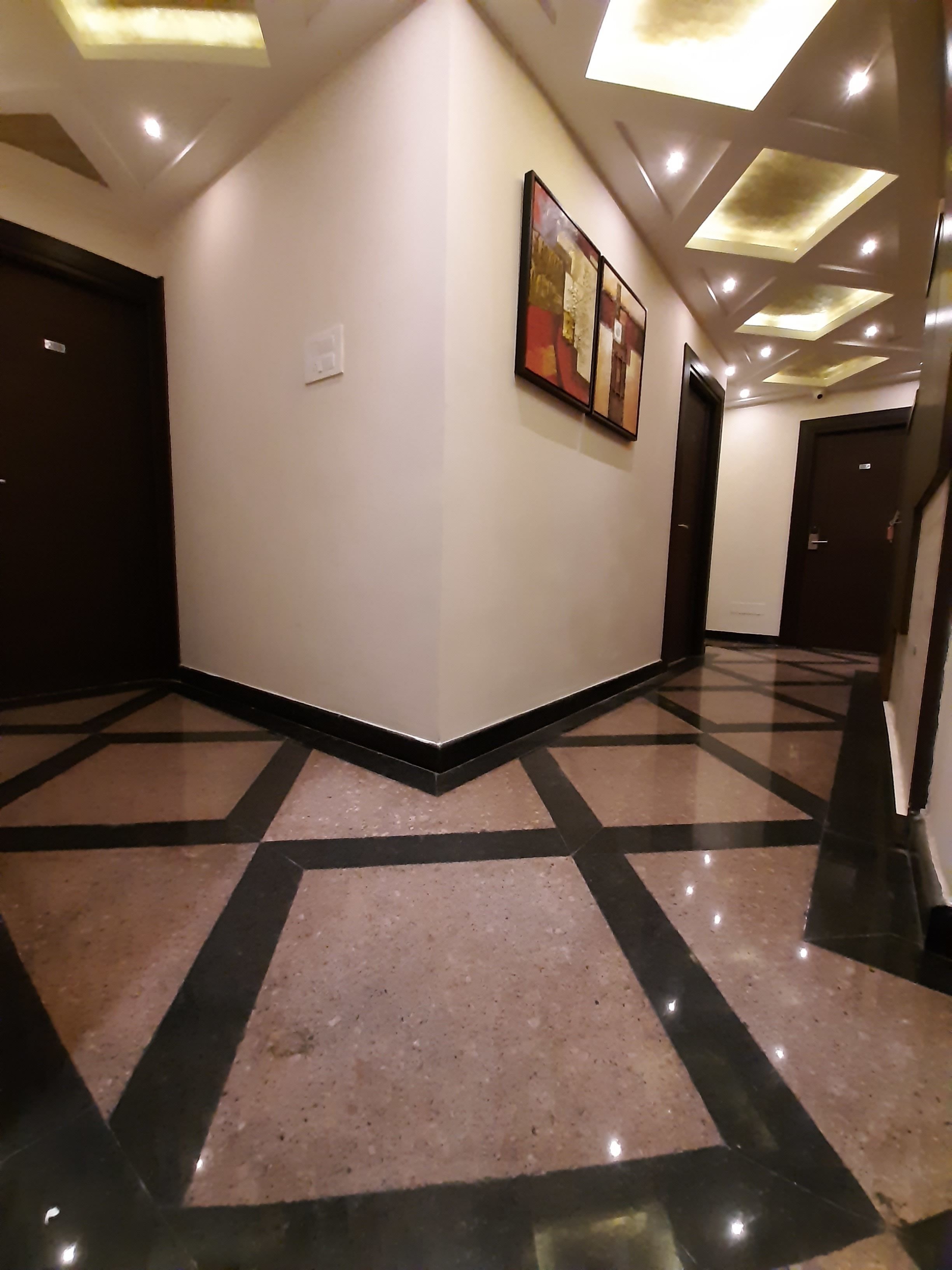 A hallway with a geometric patterned floor, recessed ceiling lights, and a framed artwork on the wall.
