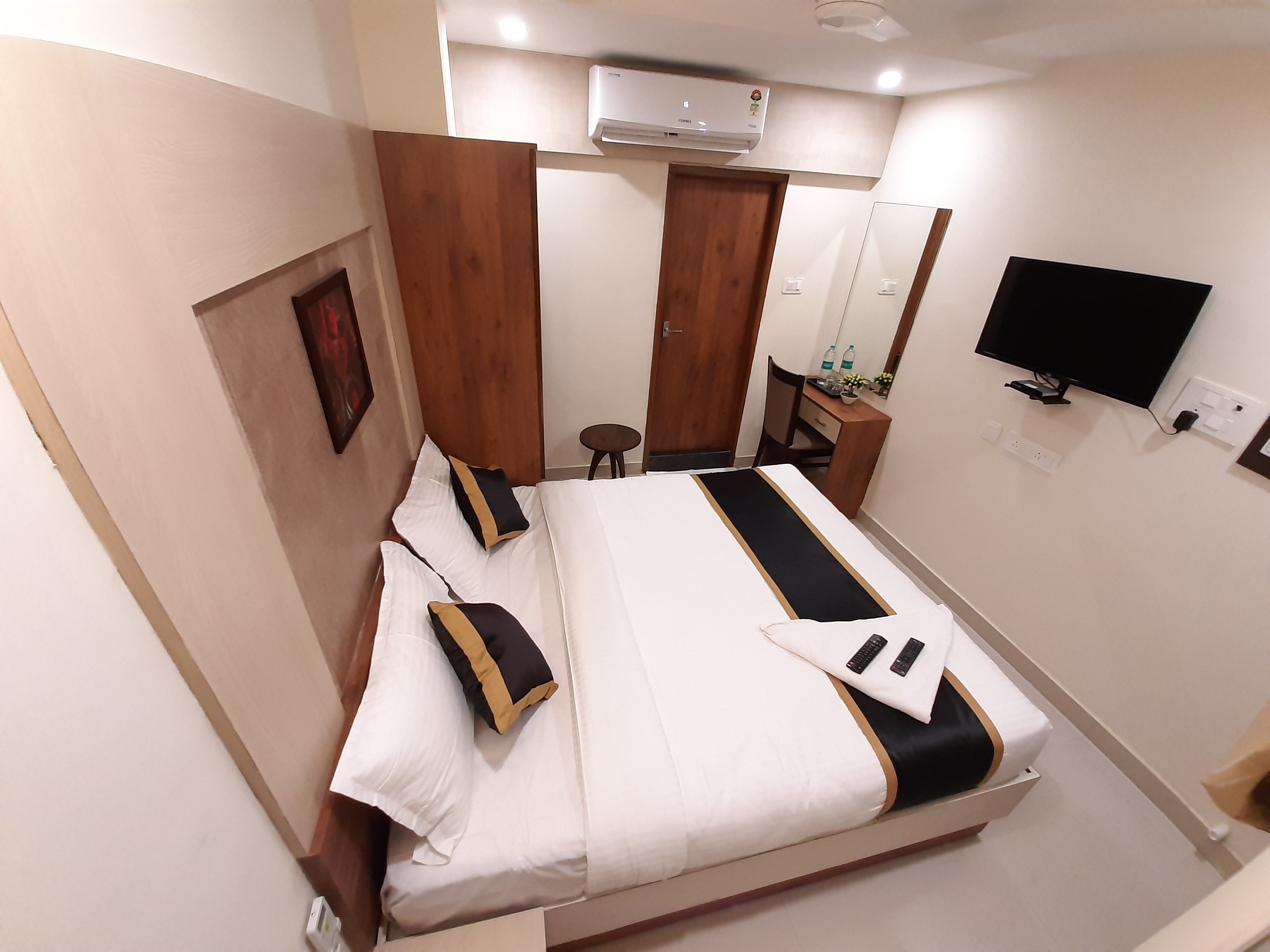 A neatly arranged bedroom with a bed, a desk, a chair, a TV, and an air conditioning unit.