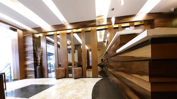A modern lobby with a marble floor, wooden paneling, and a staircase leading to upper floors. - Liza Regency (Chennai)