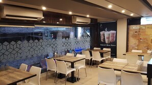A restaurant interior with tiled walls, white chairs, and wooden tables. - Liza Regency (Chennai)