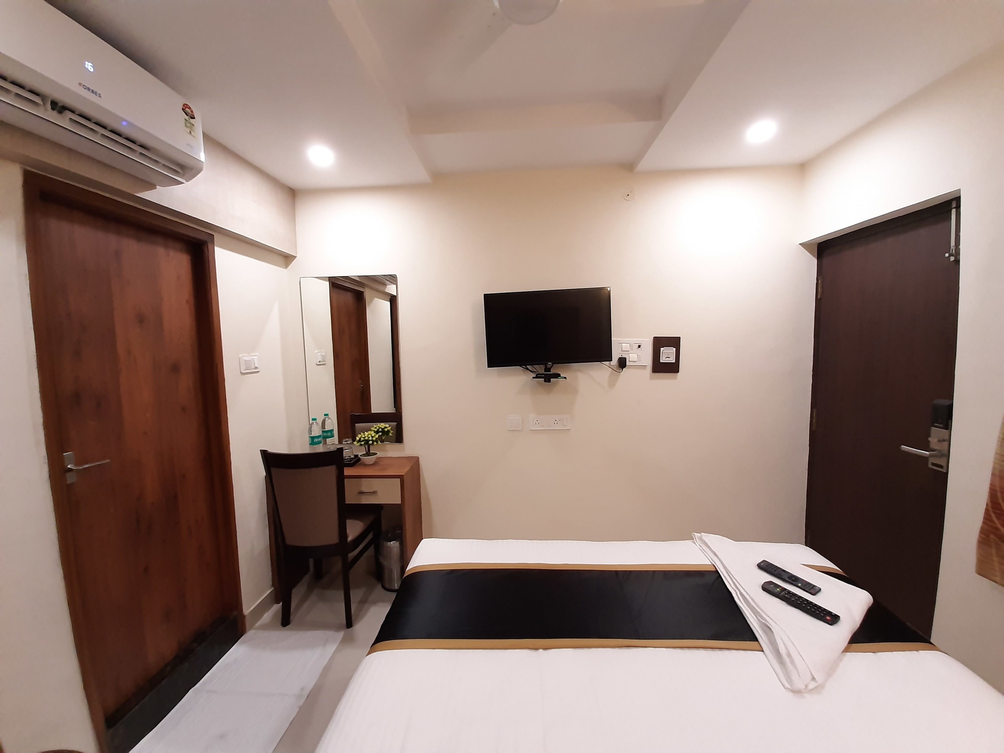 A hotel room with a bed, a desk with a chair, a television, and an air conditioning unit.