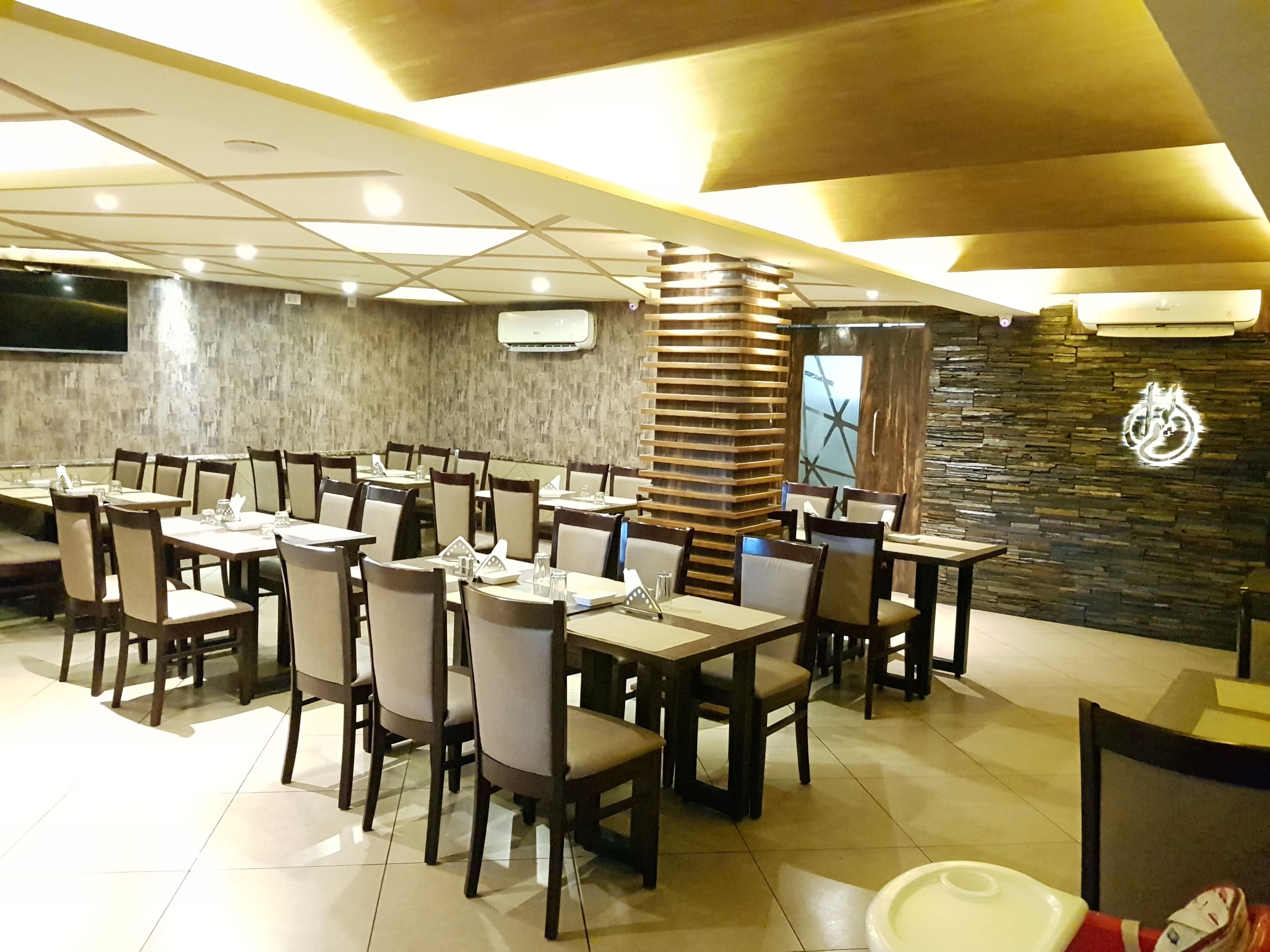 Un restaurant doté de nombreuses tables et chaises, d’un mur en pierre orné d’un logo et d’un plafond pourvu d’un éclairage encastré.