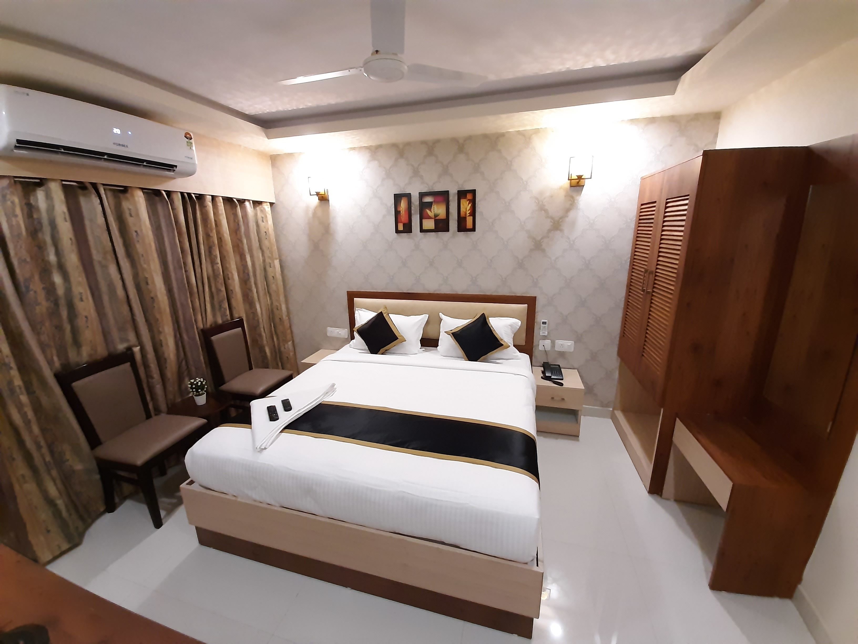 Une chambre d’hôtel équipée d’un grand lit, d’un bureau, d’une chaise, d’un climatiseur, d’un ventilateur de plafond et d’une armoire.