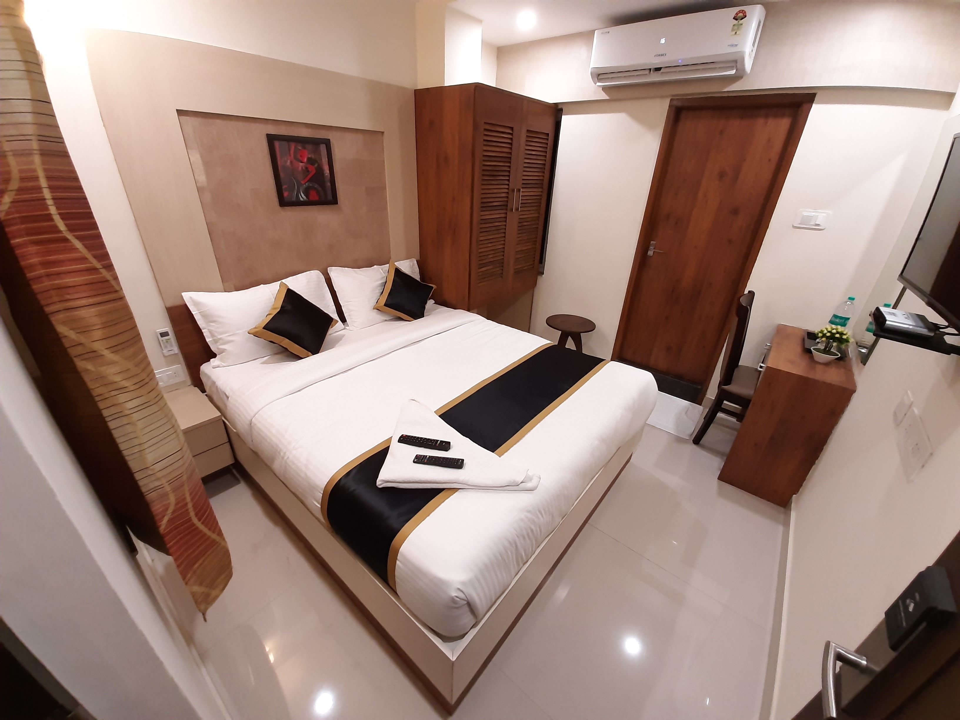 A hotel room with a bed, bedside table, TV, and an air conditioning unit.