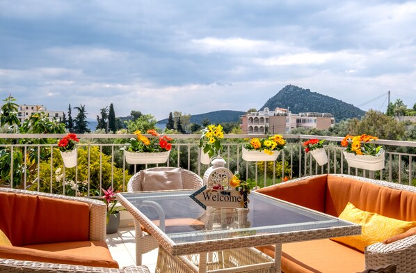 A balcony with wicker furniture, a glass table, and flower planters.