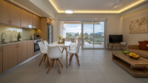 A modern kitchen with a dining area, a balcony with a TV, and a living room with a sofa and a painting. - Sirena Tolo Luxury Apartment (Nafplio)