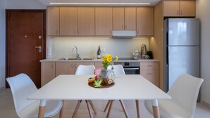 A modern kitchen with wooden cabinets, a stainless steel refrigerator, and a dining area with a white table and chairs. - Sirena Tolo Luxury Apartment (Nafplio)