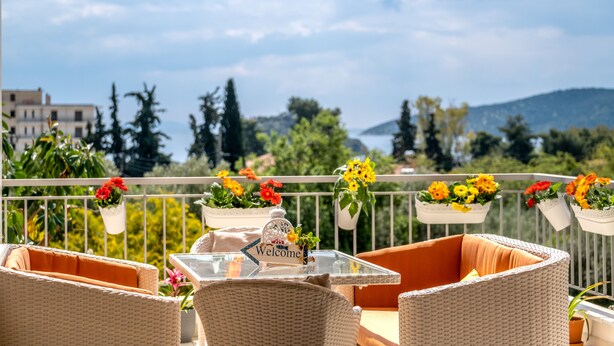 A balcony with wicker furniture, flower planters, and a welcome sign. - Sirena Tolo Luxury Apartment (Nafplio)