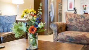 Een woonkamer met een bloemstuk op een houten salontafel, een bank en een lamp op de achtergrond.