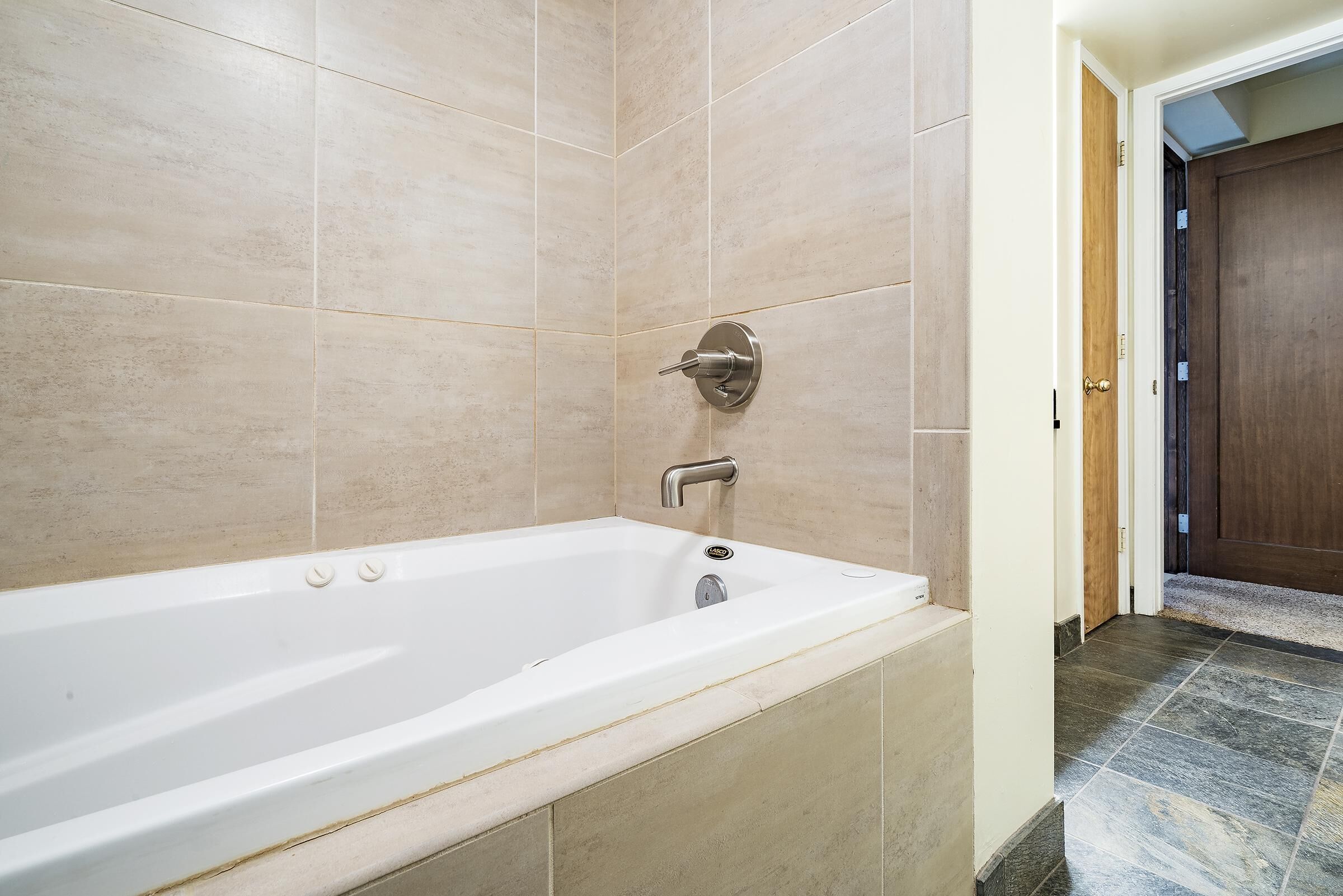 Un baño moderno con una bañera independiente, paredes de azulejos y una puerta de madera.