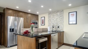 Een moderne keuken met een centraal eiland, roestvrijstalen apparatuur, houten kastjes en een betegelde achterwand.
