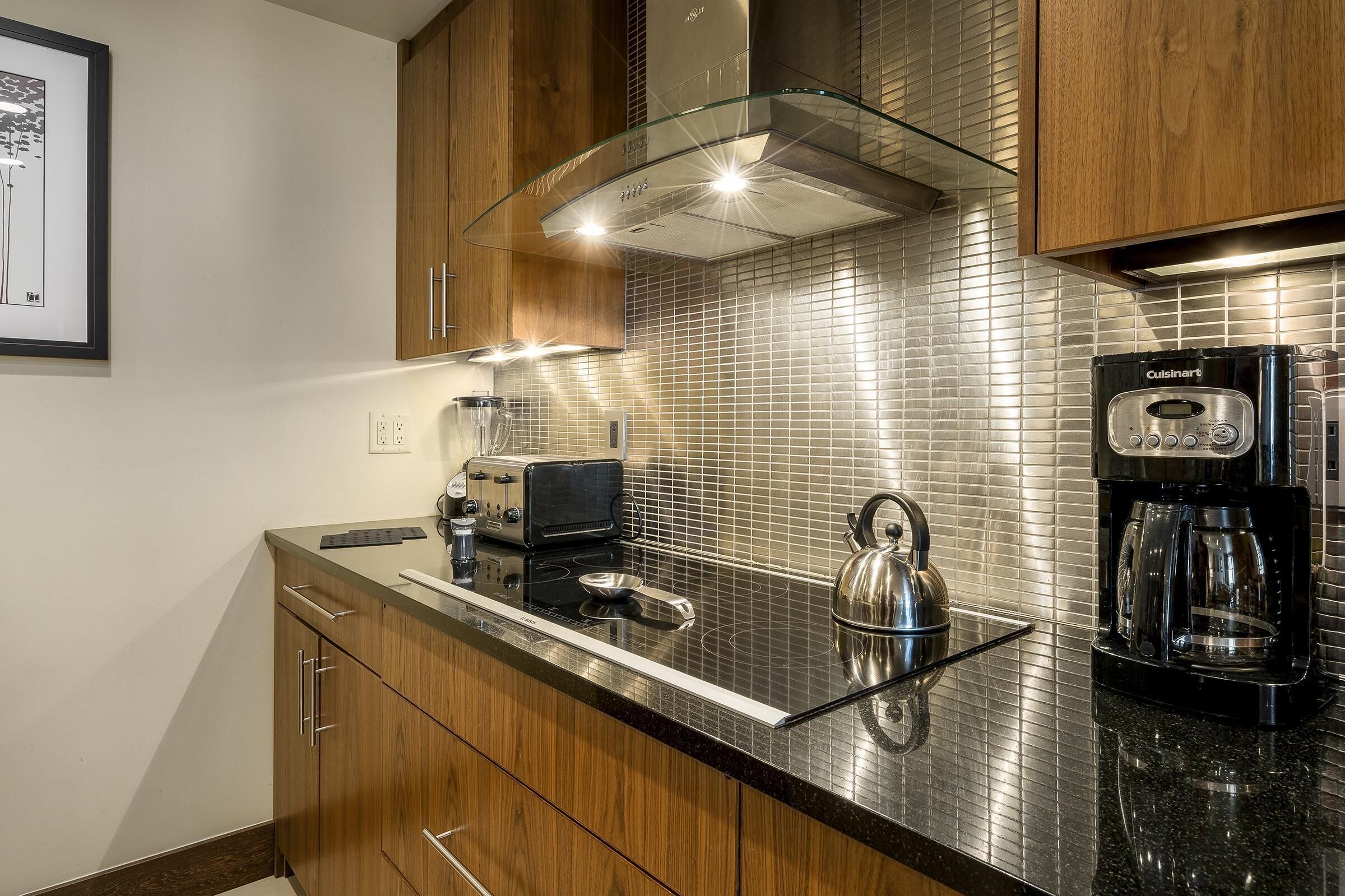 A modern kitchen with wooden cabinets, a glass range hood, a Cuisinart coffee maker, and a kettle on the countertop.