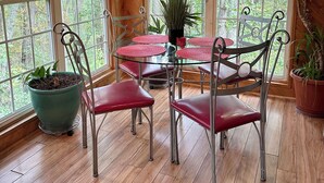 Una habitación con paneles de madera, una mesa de vidrio y sillas de metal, ventanas amplias y plantas en macetas.