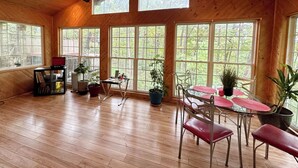Una habitación amplia con piso de madera, ventanas grandes, ventilador de techo y un comedor con mesa y sillas.
