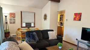 Una sala de estar con sofá, mesa de centro, televisor y comedor con mesa y sillas.