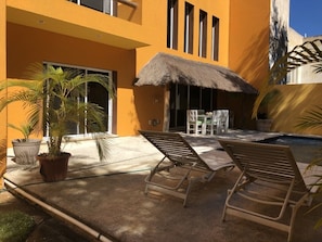 Relax in style with a lounge chair under a shaded umbrella, surrounded by lush greenery and a nearby pool.
