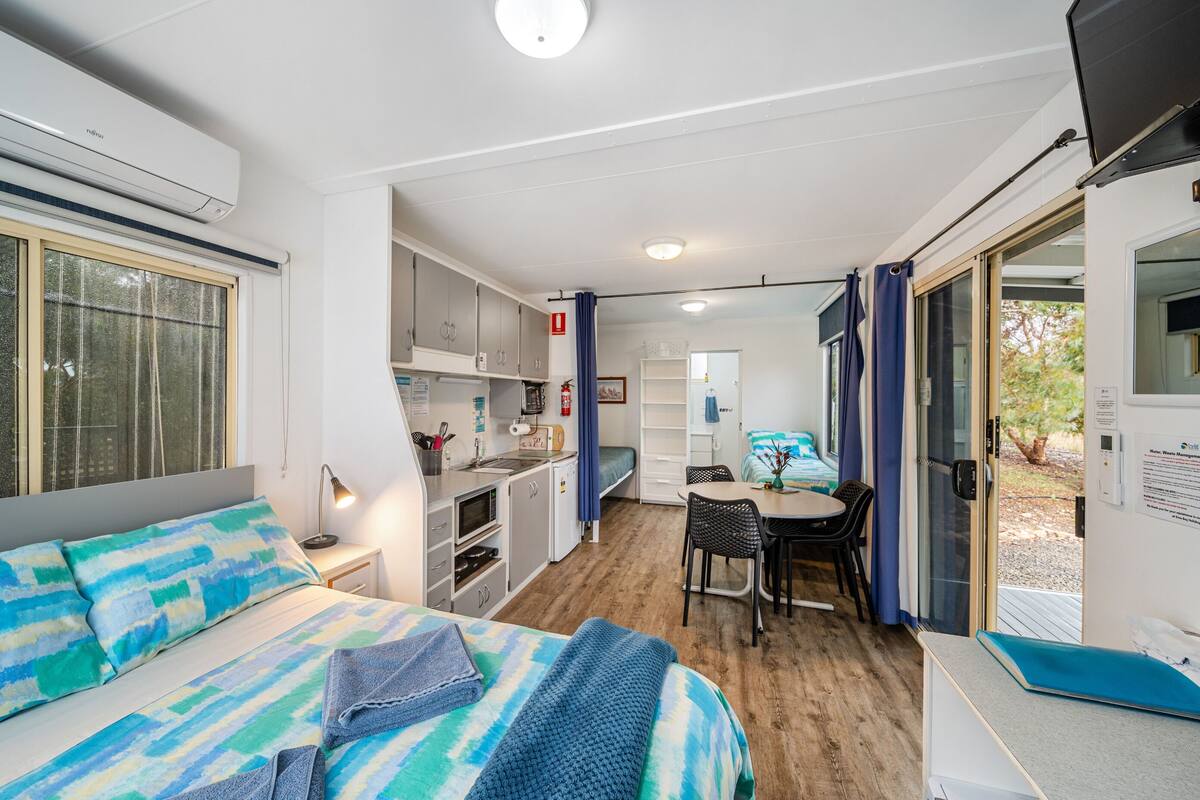 A compact, well-lit room with a bed, kitchenette, and a small dining area.