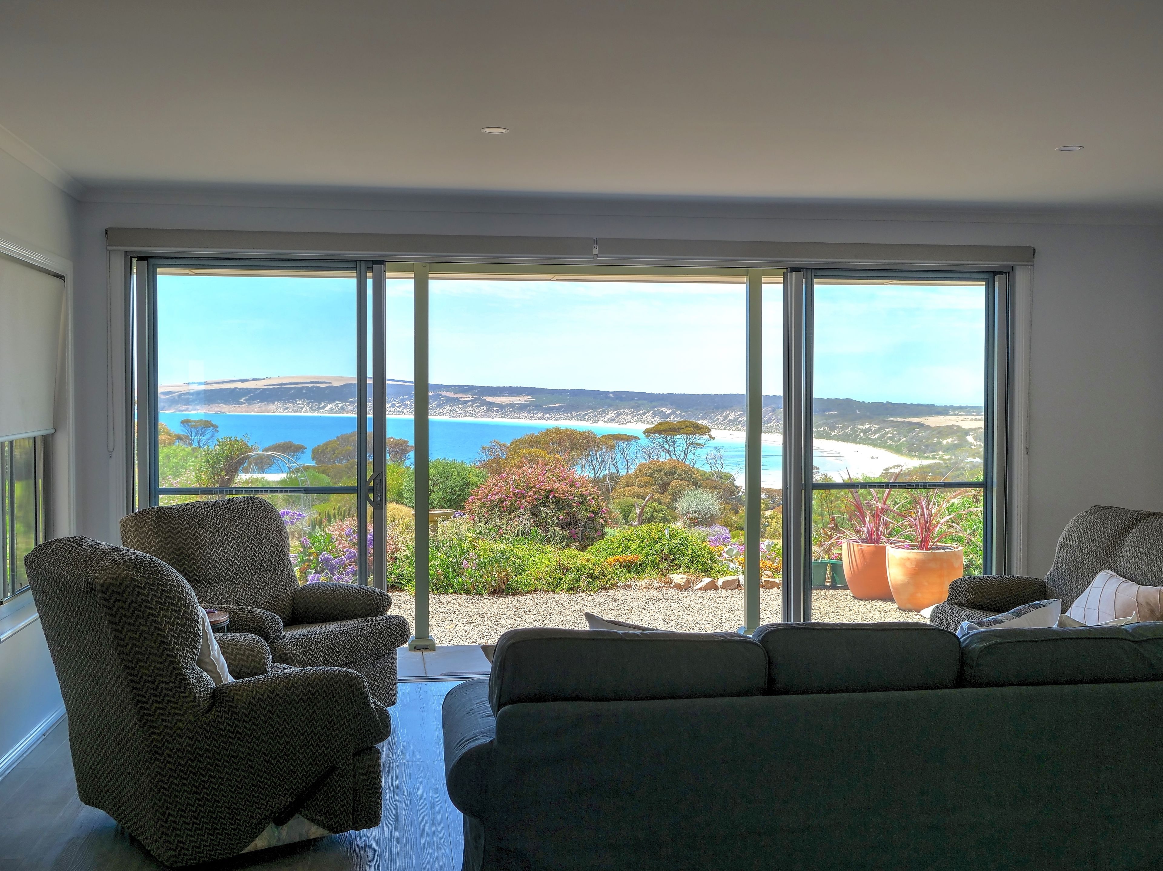 A spacious room with a large sliding glass door leading to a balcony with a view of the sea and greenery.