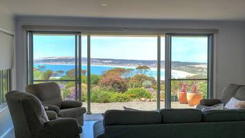 A spacious room with a large sliding glass door leading to a balcony with a view of the sea and greenery.